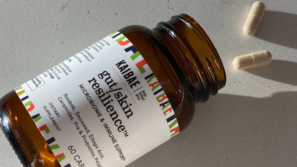 KAIBAE gut/skin resilience supplement with 2 capsules spilling out of bottle on to the counter top. Gut/skin resilience is a polyphenol rich blend with Baobab and Pomegranate and other nutrients that benefit healthy glowing skin