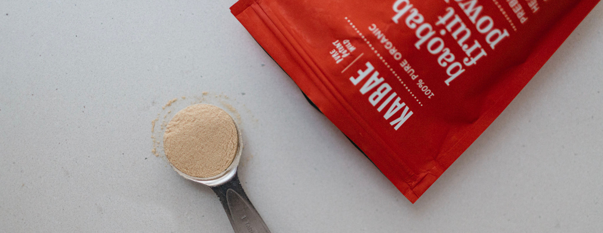 Baobab powder in a bright red pouch on its side with a measuring spoon of Baobab 