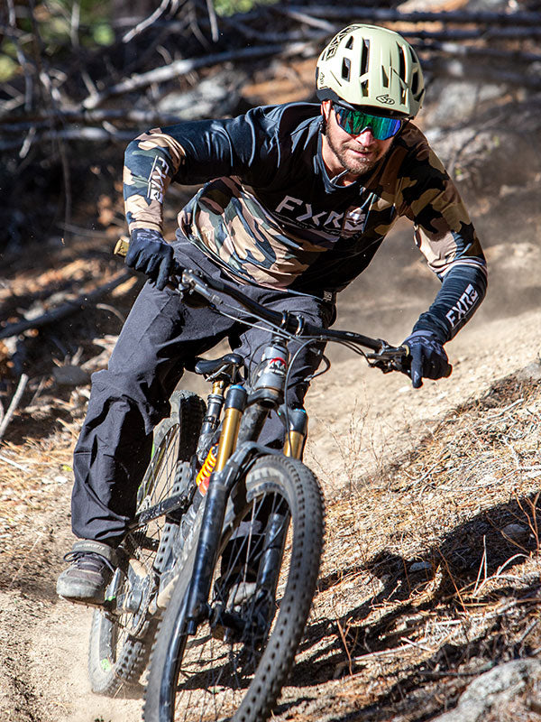 Low angled shot of a guy on a mountain bike wearing FXR's new Proflex UPF Shirt in HiVis fade/blue fade colorway