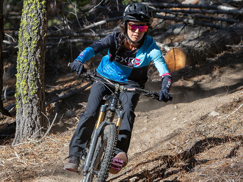 Full angled shot of a lady in FXR's Women's Attack UPF Longsleeve in Sky Fade/Black colorway riding her mountain bike