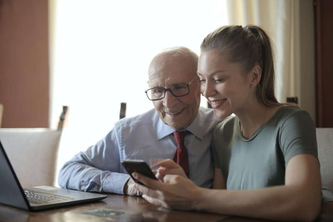 Older gentleman and younger lady smiling, looking at phone