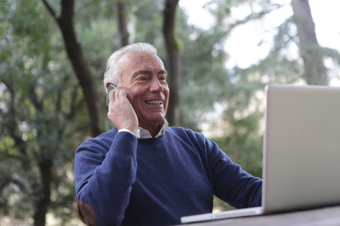 Older man smiling on his phone and laptop doing work