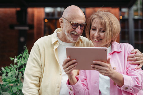 An elderly couple smiling, looking at an iPad