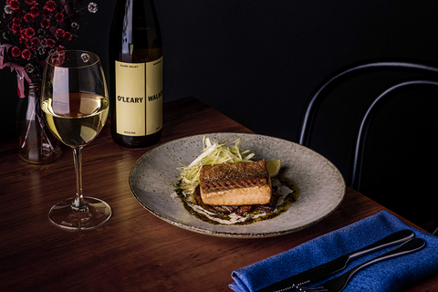 Bottle of Riesling stands next to half full glass, alongside pan seared salmon and fennel on ceramic plate