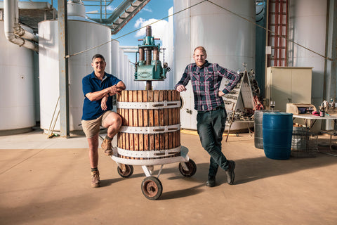 Winemakers Luke Broadbent and Jack Walker stand alongside a traditional basket press