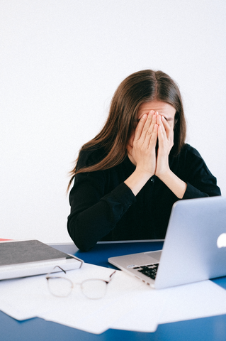 woman looking stressed covering face at laptop computer