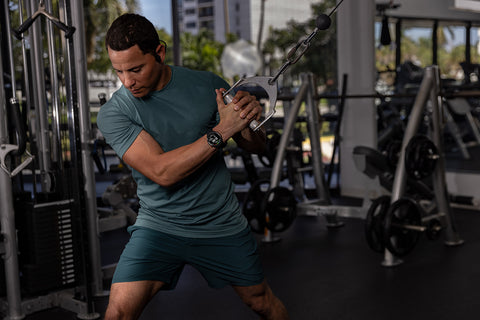 A man working out in the gym on exercise equipment while wearing a Garmin Approach S70 golf watch