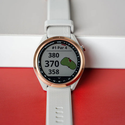 A rose gold and white Garmin Approach S42 leaning against a white wall and red floor at PlayBetter