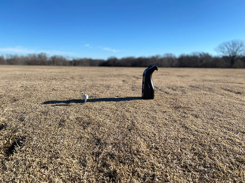 The Bushnell Launch Pro at the golf range with a golf ball on a tee in front of it on brown winter grass with a blue sky in the background