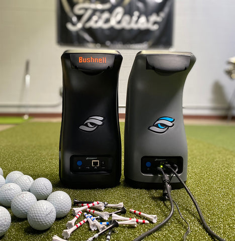 Rear view of the Launch Pro and GC3 launch monitor units side by side with some golf balls on a golf mat