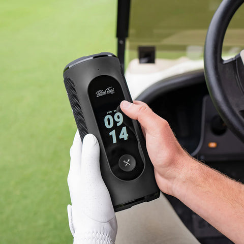 The Blue Tees Player+ Touchscreen golf speaker being held in a golfers hands in a golf cart on the course