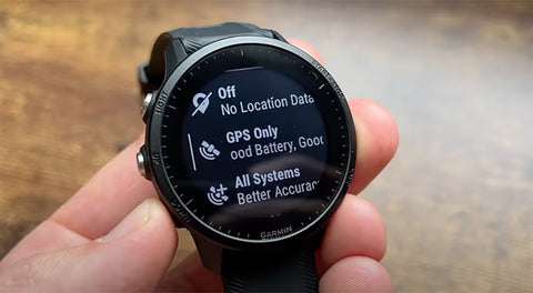 A hand holding a black Garmin Forerunner 955 with GPS options on the display