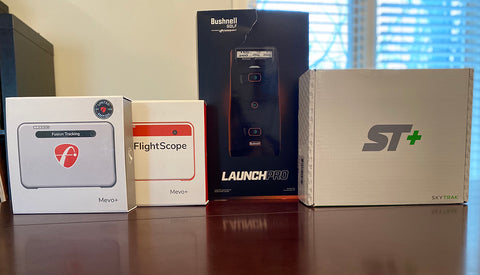 The FlightScope Mevo+ Limited Edition and Mevo+, Bushnell Launch Pro , and SkyTrak+ in boxes on a table with a window behind