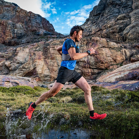 A man running in a valley in the mountains wearing a Garmin Enduro 2 GPS watch