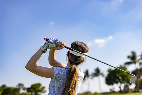 Rear, waist-up view of a woman swinging on the golf wearing a Garmin Approach S70 golf watch course