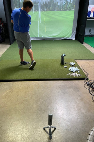 Golf reviewer Marc in an indoor golf simulator showing him taking a shot with the Rapsodo MLM2PRO behind him and Foresight GC3 next to him, comparing the accuracy of the two