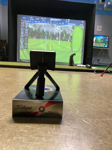 The Garmin Approach R10 sitting on a box in front of a golf simulator