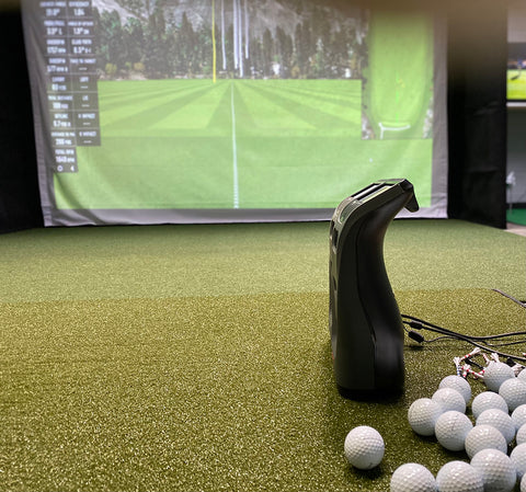 A Bushnell Launch Pro on a golf mat next to a bunch of golf balls in an indoor golf simulator