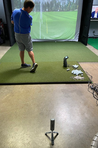 The Rapsodo MLM2PRO set up behind golf reviewer Marc standing next to a Foresight Sport GC3 in a golf simulator