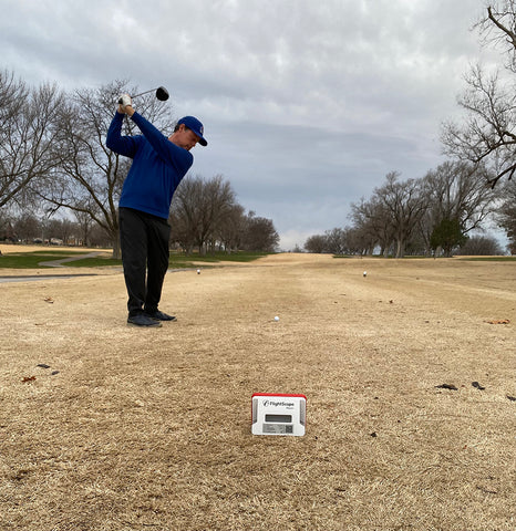 Marc swinging his driver on the golf course with the Mevo+ set up behind him