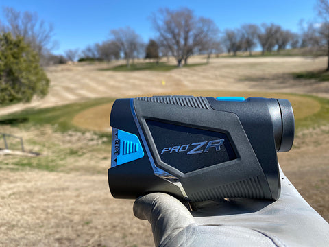 The Shot Scope Pro ZR rangefinder held in golf reviewer Marc's golf-gloved hand on the course