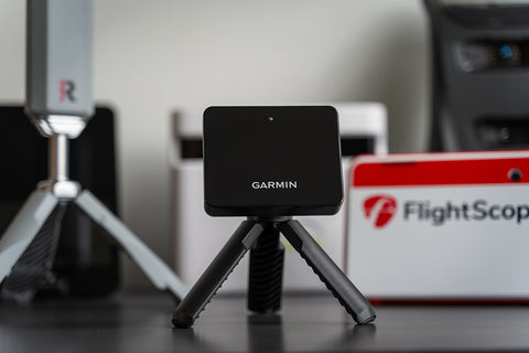 The Garmin Approach R10 unit sitting in front of other golf launch monitors, including the Rapsodo MLM2PRO, FlightScope Mevo+, SkyTrak+ and Swing Caddie SC4
