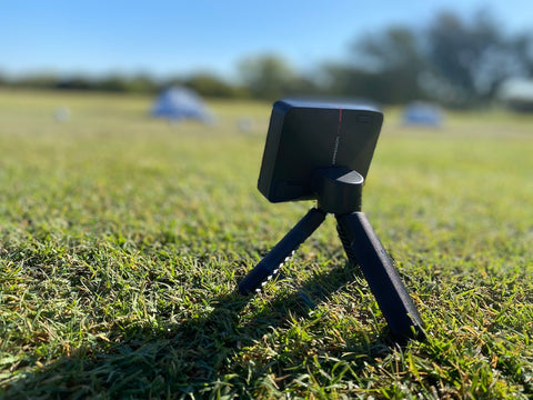 A rear-angled view of the Garmin Approach R10 standing on the grass at the golf range