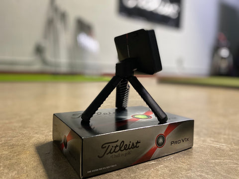 The Garmin Approach R10 sitting on a Titleist golf ball box in a golf simulator