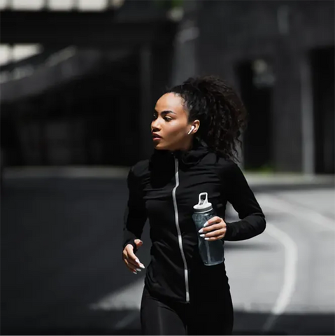 A woman running in the city with earbuds in her ears and water bottle in her hand