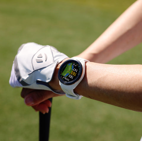 A white 42 mm Garmin Approach S70 golf watch on a woman's wrist with golf glove on the hand