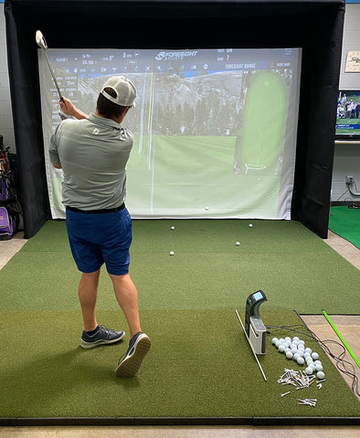 Marc post swing in an indoor golf simulator facing the impact screen with SkyTrak virtual golf software on itusing the SkyTrak+ and GC3