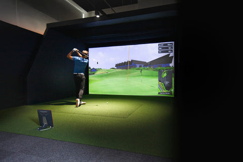 A golfer swinging in a golf simulator with a Trackman launch monitor standing behind him