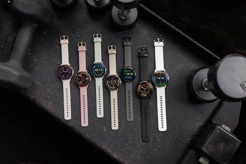 Several colors and sizes of the Garmin Venu 3/3S watches laid out side-by-side on a dark desk