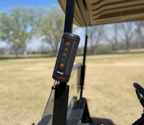 The Bushnell Wingman 2 golf speaker attached to a golf cart by the devices magnet