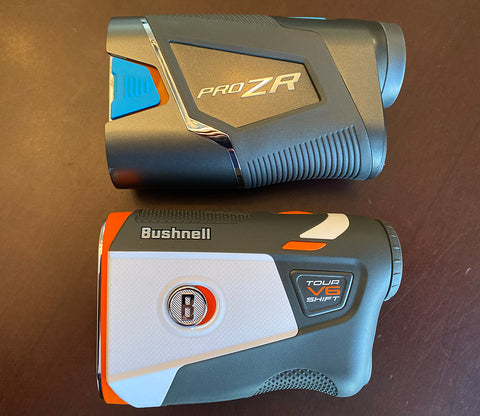 The Shot Scope PRO ZR and Bushnell Tour V6 rangefinders laying next to each other on a table