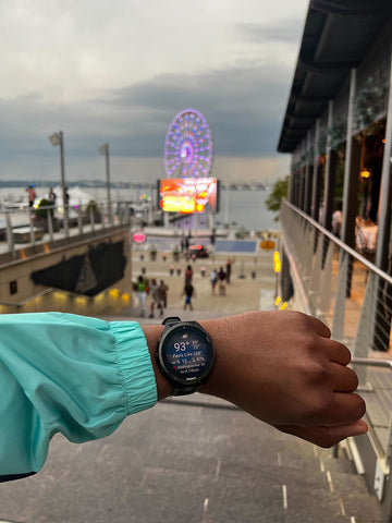 A forarm with a Garmin Forerunner 965 on the wrist with a Baltimore pier in the foreground