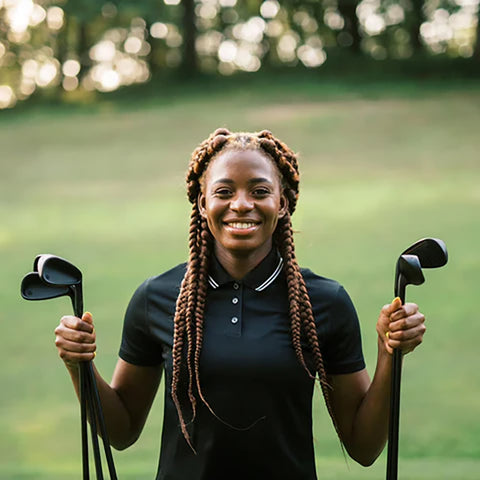 golfer holding several golf clubs in each hand while smiling on the golf course