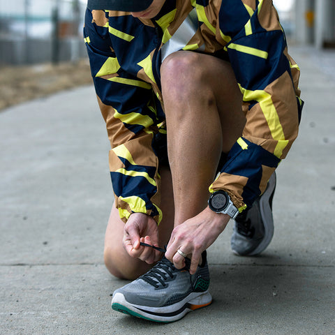 A runner tying their shoe outside with a Forerunner 255 on their wrist