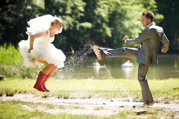 A childish bride wearing wellys and groom jump in puddles after a unique wedding