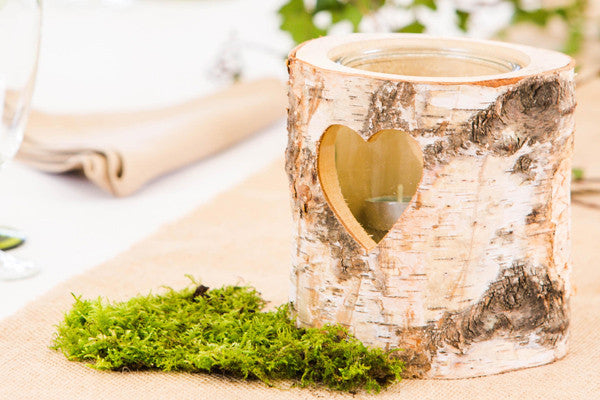 A rustic wood slice candle holder surrounded by moss decorates a nature themed wedding reception