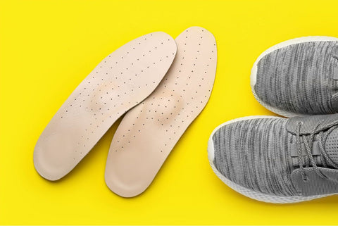 A pair of insoles next to a pair of women's shoes on a bright yellow background.