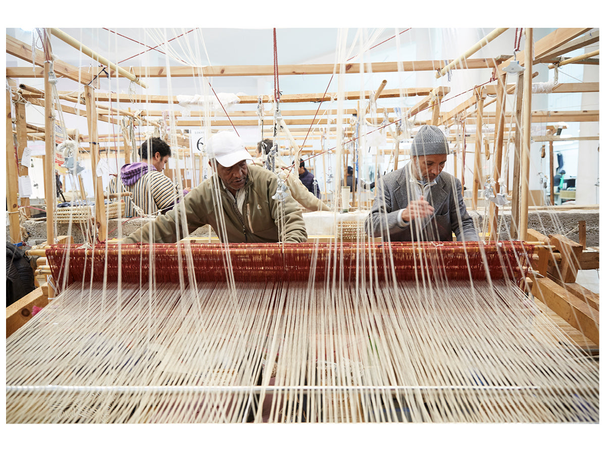 This image shows two male artisans working together at a large weaving loom in the Marrakshi Life atelier.