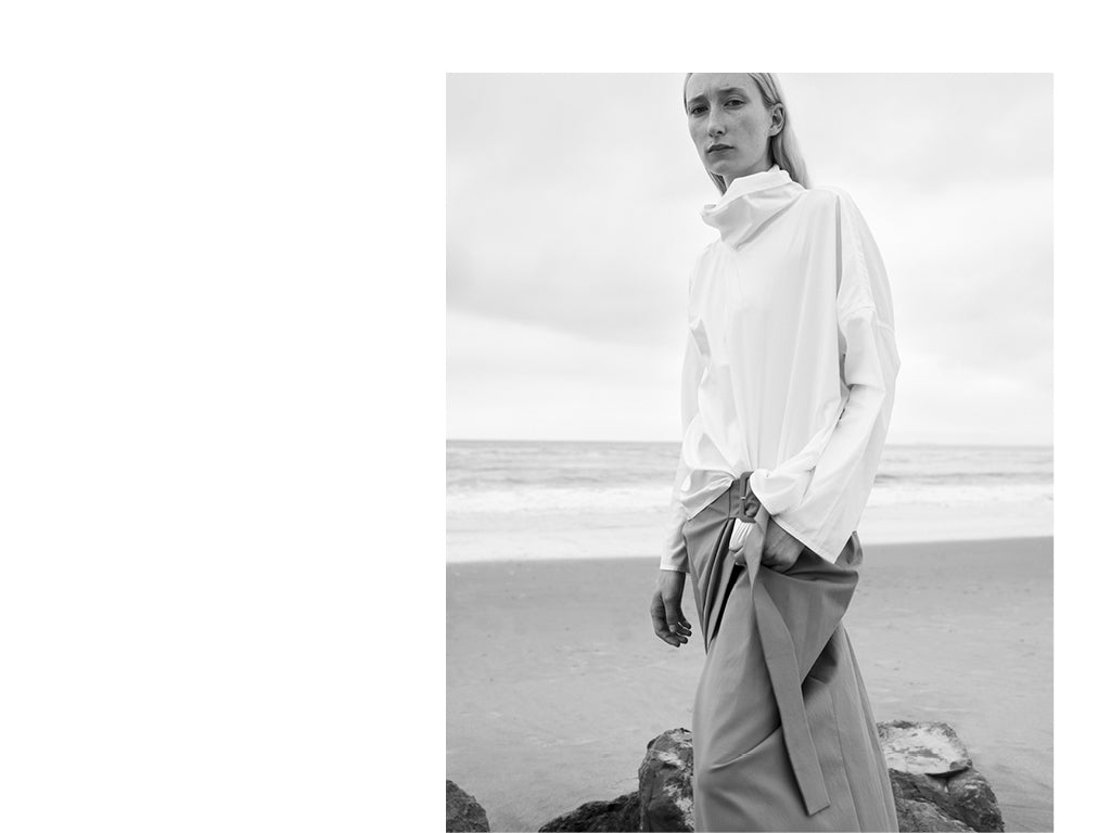 A cropped Black and White image of a woman wearing a long sleeve cotton shirt by Sofie D'Hoore with a wrap skirt by Rejina Pyo.