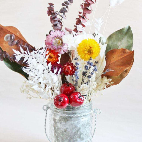 A dried flower arrangement in a glass jar on a white background