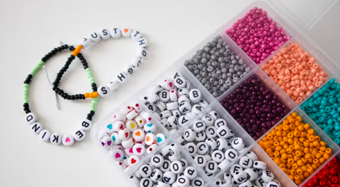 Two beaded bracelets next to a box full of beads on a white background