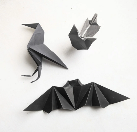 Three origami pieces -- a bat, a raven, and a pumpkin -- made with black paper.