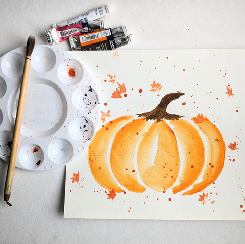 A watercolor painting of a pumpkin, next to tubes of paint, a palette, and a paintbrush