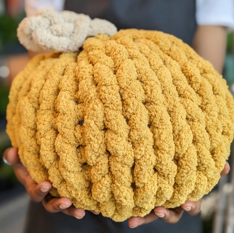 A person holding a yellow knitted pumpkin