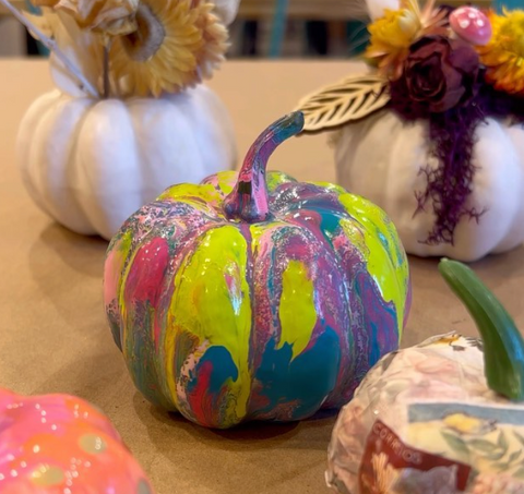 One multi-colored painted pumpkin in the middle of several other decorated pumpkins