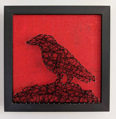 A red canvas with string art that resembles the silhouette of a raven standing on a rock